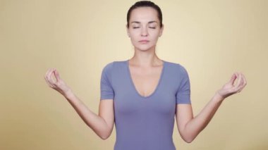 Beyaz tenli çekici kadın bej arka planda meditasyon yapıyor.