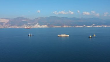 Güneşli bir günde deniz limanından ayrılan büyük kargo gemisinin hava görüntüsü.