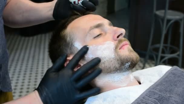 Peluquero corta la barba de los clientes con una recortadora de barba profesional en una barbería sobre fondo claro, primer plano . — Vídeo de stock