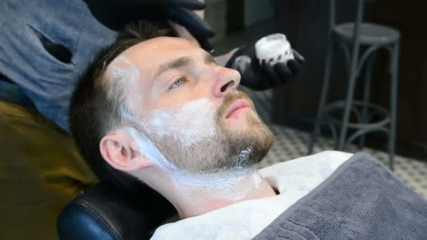 Peluquero corta la barba de los clientes con una recortadora de barba profesional en una barbería sobre fondo claro, primer plano . — Vídeos de Stock