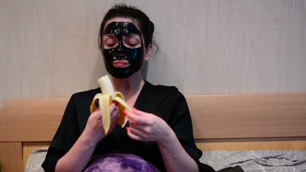顔に黒いマスクを持つ少女は バナナを食べる — ストック動画