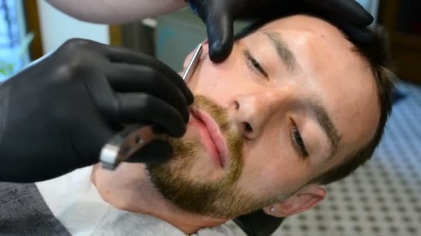 剃胡子用直剃刀刮 在理发店里关门剃胡子 男性胡须风格 理发师剃须时髦的人脸 — 图库视频影像