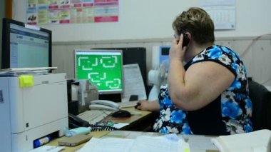 İşçisi kadın Asansör bakım bölümü kontrol odasında üzerinde konuşuyor. Orada birkaç monitörler ve bir telefon.