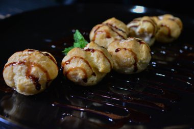 Pasta krema ile doldurulmuş ve tepesinde siyah bir tabak içinde çikolata soslu kek profiterol taze krema puffs. popüler Farsça tatlı