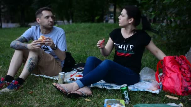 俄罗斯莫斯科 2018年7月21日 年轻人吃三明治和喝啤酒 在草坪野餐 坐在公园的绿草上 快乐的青少年有一些食物 — 图库视频影像