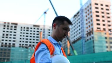 Yetişkin mühendis veya mimar bir tablet işlemi kullanır. Bir ileti yazar veya bir çizim denetler. Arka planı yapıdır. İnşaatçılar beton ve cam modern konut bina inşa ediyoruz.
