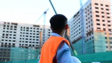 Yetişkin mühendis veya mimar bir tablet işlemi kullanır. Bir ileti yazar veya bir çizim denetler. Arka planı yapıdır. İnşaatçılar beton ve cam modern konut bina inşa ediyoruz.
