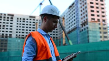 Yetişkin mühendis veya mimar bir tablet işlemi kullanır. Bir ileti yazar veya bir çizim denetler. Arka planı yapıdır. İnşaatçılar beton ve cam modern konut bina inşa ediyoruz.