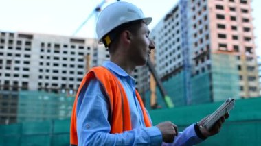Yetişkin mühendis veya mimar bir tablet işlemi kullanır. Bir ileti yazar veya bir çizim denetler. Arka planı yapıdır. İnşaatçılar beton ve cam modern konut bina inşa ediyoruz.