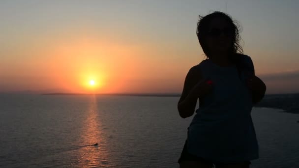Aktivní mladá žena silueta taneční venku na západ slunce s slunce svítit za ní na horizont. — Stock video