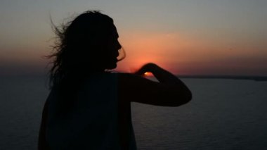 gün batımı bir arka plan bir Bayan dansları akşamları, saçları rüzgarda çırpınan kum üzerinde hareket eden bir kadına silüeti