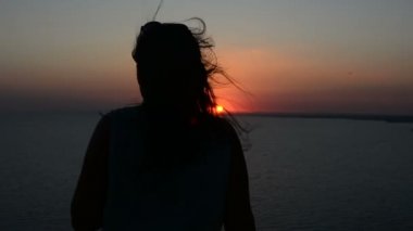 gün batımı bir arka plan bir Bayan dansları akşamları, saçları rüzgarda çırpınan kum üzerinde hareket eden bir kadına silüeti