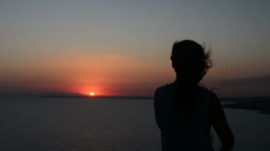 gün batımı bir arka plan bir Bayan dansları akşamları, saçları rüzgarda çırpınan kum üzerinde hareket eden bir kadına silüeti