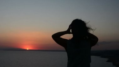 gün batımı bir arka plan bir Bayan dansları akşamları, saçları rüzgarda çırpınan kum üzerinde hareket eden bir kadına silüeti