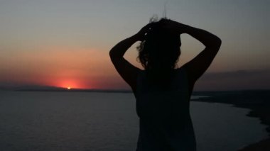 gün batımı bir arka plan bir Bayan dansları akşamları, saçları rüzgarda çırpınan kum üzerinde hareket eden bir kadına silüeti