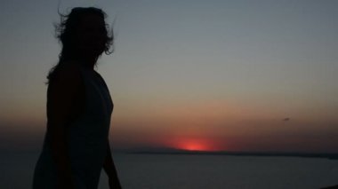 gün batımı bir arka plan bir Bayan dansları akşamları, saçları rüzgarda çırpınan kum üzerinde hareket eden bir kadına silüeti