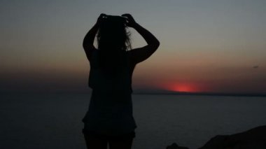 gün batımı bir arka plan bir Bayan dansları akşamları, saçları rüzgarda çırpınan kum üzerinde hareket eden bir kadına silüeti