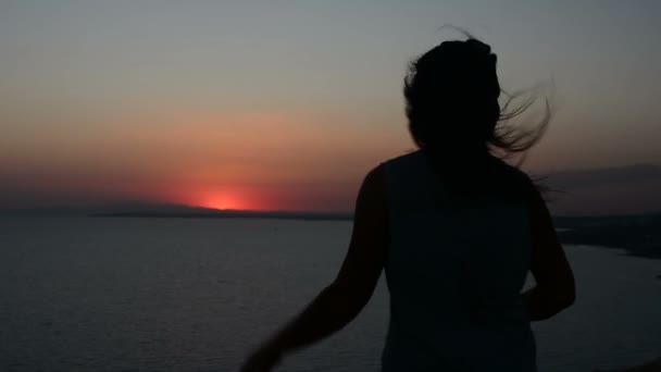 Silhouet van een vrouw die tegen een zonsondergang achtergrond, een dame dansen op het zand in de avond, haar haren wapperen in de wind beweegt — Stockvideo