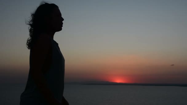 Silhouette d'une femme qui se déplace sur un fond de coucher de soleil, une dame danse sur le sable le soir, ses cheveux flottent dans le vent — Video