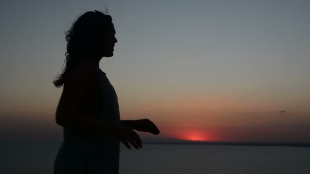 Silhouet van een vrouw die tegen een zonsondergang achtergrond, een dame dansen op het zand in de avond, haar haren wapperen in de wind beweegt — Stockvideo