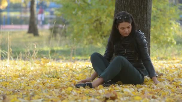 秋の公園笑顔でツリーの下に座って美しい少女 — ストック動画