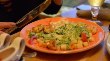 Sezar salata kırmızı maşa, parmesan peyniri, sos, plaka üzerinde makro closeup maşa, hareketli, arka planda yeme insanlar