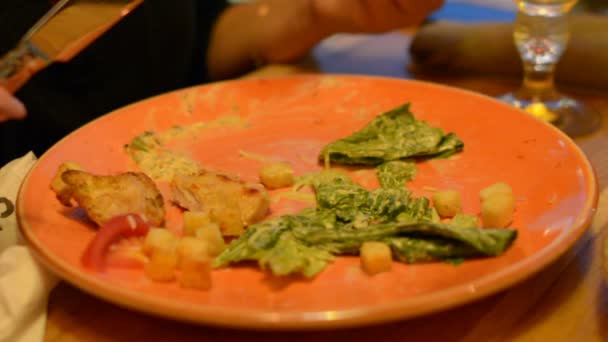 在盘子里的凯撒沙拉的宏观特写镜头与红色的钳子 帕玛森奶酪 人移动 吃在背景 — 图库视频影像