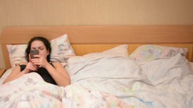 Kadın yatağında akıllı telefon kullanıyor.