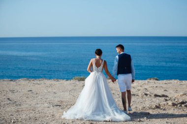 Genç gelin ve damat sahilde yürüyüş, Öpüşme ve sahip eğlenceli, düğün töreni kayalar ve deniz yakınında gülümseyen güzel. Kıbrıs Sahil düğün töreni