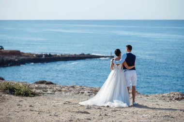 Genç gelin ve damat sahilde yürüyüş, Öpüşme ve sahip eğlenceli, düğün töreni kayalar ve deniz yakınında gülümseyen güzel. Kıbrıs Sahil düğün töreni