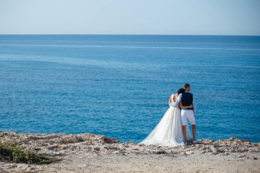 Genç gelin ve damat sahilde yürüyüş, Öpüşme ve sahip eğlenceli, düğün töreni kayalar ve deniz yakınında gülümseyen güzel. Kıbrıs Sahil düğün töreni