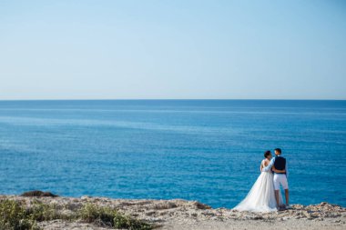 Genç gelin ve damat sahilde yürüyüş, Öpüşme ve sahip eğlenceli, düğün töreni kayalar ve deniz yakınında gülümseyen güzel. Kıbrıs Sahil düğün töreni
