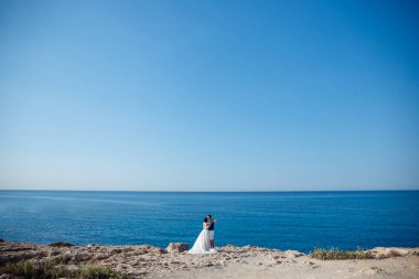 Genç gelin ve damat sahilde yürüyüş, Öpüşme ve sahip eğlenceli, düğün töreni kayalar ve deniz yakınında gülümseyen güzel. Kıbrıs Sahil düğün töreni