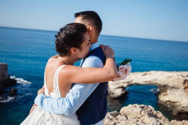 Genç gelin ve damat sahilde yürüyüş, Öpüşme ve sahip eğlenceli, düğün töreni kayalar ve deniz yakınında gülümseyen güzel. Kıbrıs Sahil düğün töreni