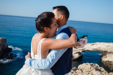 Genç gelin ve damat sahilde yürüyüş, Öpüşme ve sahip eğlenceli, düğün töreni kayalar ve deniz yakınında gülümseyen güzel. Kıbrıs Sahil düğün töreni