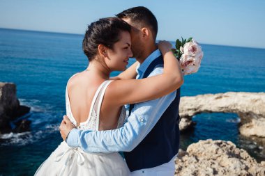 Genç gelin ve damat sahilde yürüyüş, Öpüşme ve sahip eğlenceli, düğün töreni kayalar ve deniz yakınında gülümseyen güzel. Kıbrıs Sahil düğün töreni