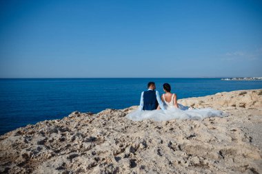 Genç gelin ve damat sahilde yürüyüş, Öpüşme ve sahip eğlenceli, düğün töreni kayalar ve deniz yakınında gülümseyen güzel. Kıbrıs Sahil düğün töreni