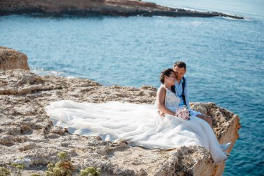 Genç gelin ve damat sahilde yürüyüş, Öpüşme ve sahip eğlenceli, düğün töreni kayalar ve deniz yakınında gülümseyen güzel. Kıbrıs Sahil düğün töreni