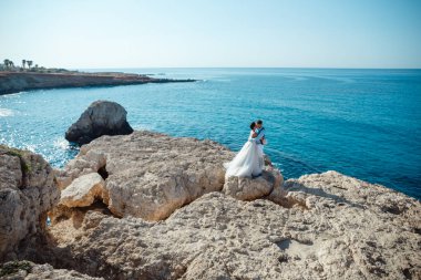 Genç gelin ve damat sahilde yürüyüş, Öpüşme ve sahip eğlenceli, düğün töreni kayalar ve deniz yakınında gülümseyen güzel. Kıbrıs Sahil düğün töreni