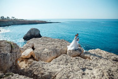 Genç gelin ve damat sahilde yürüyüş, Öpüşme ve sahip eğlenceli, düğün töreni kayalar ve deniz yakınında gülümseyen güzel. Kıbrıs Sahil düğün töreni