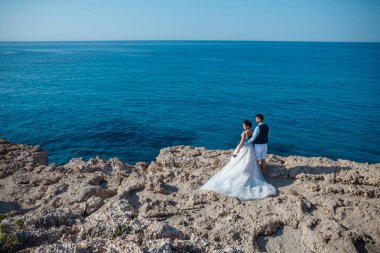 Genç gelin ve damat sahilde yürüyüş, Öpüşme ve sahip eğlenceli, düğün töreni kayalar ve deniz yakınında gülümseyen güzel. Kıbrıs Sahil düğün töreni