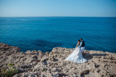 Genç gelin ve damat sahilde yürüyüş, Öpüşme ve sahip eğlenceli, düğün töreni kayalar ve deniz yakınında gülümseyen güzel. Kıbrıs Sahil düğün töreni