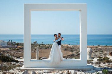 Genç gelin ve damat sahilde yürüyüş, Öpüşme ve sahip eğlenceli, düğün töreni kayalar ve deniz yakınında gülümseyen güzel. Kıbrıs Sahil düğün töreni