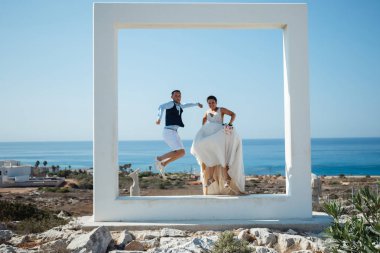 Genç gelin ve damat sahilde yürüyüş, Öpüşme ve sahip eğlenceli, düğün töreni kayalar ve deniz yakınında gülümseyen güzel. Kıbrıs Sahil düğün töreni