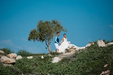 Genç gelin ve damat sahilde yürüyüş, Öpüşme ve sahip eğlenceli, düğün töreni kayalar ve deniz yakınında gülümseyen güzel. Kıbrıs Sahil düğün töreni