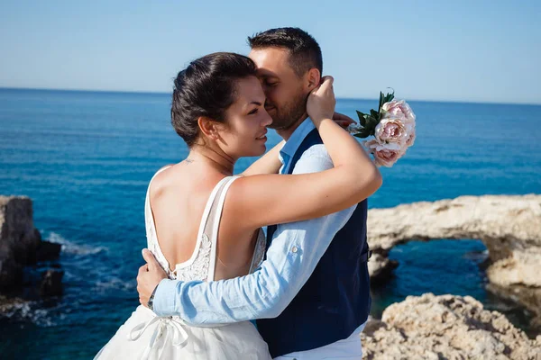 Genç gelin ve damat sahilde yürüyüş, Öpüşme ve sahip eğlenceli, düğün töreni kayalar ve deniz yakınında gülümseyen güzel. Kıbrıs Sahil düğün töreni