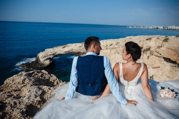 Genç gelin ve damat sahilde yürüyüş, Öpüşme ve sahip eğlenceli, düğün töreni kayalar ve deniz yakınında gülümseyen güzel. Kıbrıs Sahil düğün töreni