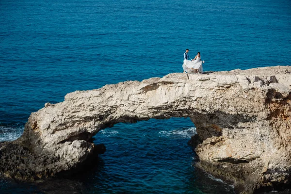 Genç gelin ve damat sahilde yürüyüş, Öpüşme ve sahip eğlenceli, düğün töreni kayalar ve deniz yakınında gülümseyen güzel. Kıbrıs Sahil düğün töreni