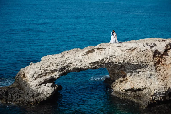 Genç gelin ve damat sahilde yürüyüş, Öpüşme ve sahip eğlenceli, düğün töreni kayalar ve deniz yakınında gülümseyen güzel. Kıbrıs Sahil düğün töreni