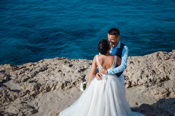 Genç gelin ve damat sahilde yürüyüş, Öpüşme ve sahip eğlenceli, düğün töreni kayalar ve deniz yakınında gülümseyen güzel. Kıbrıs Sahil düğün töreni